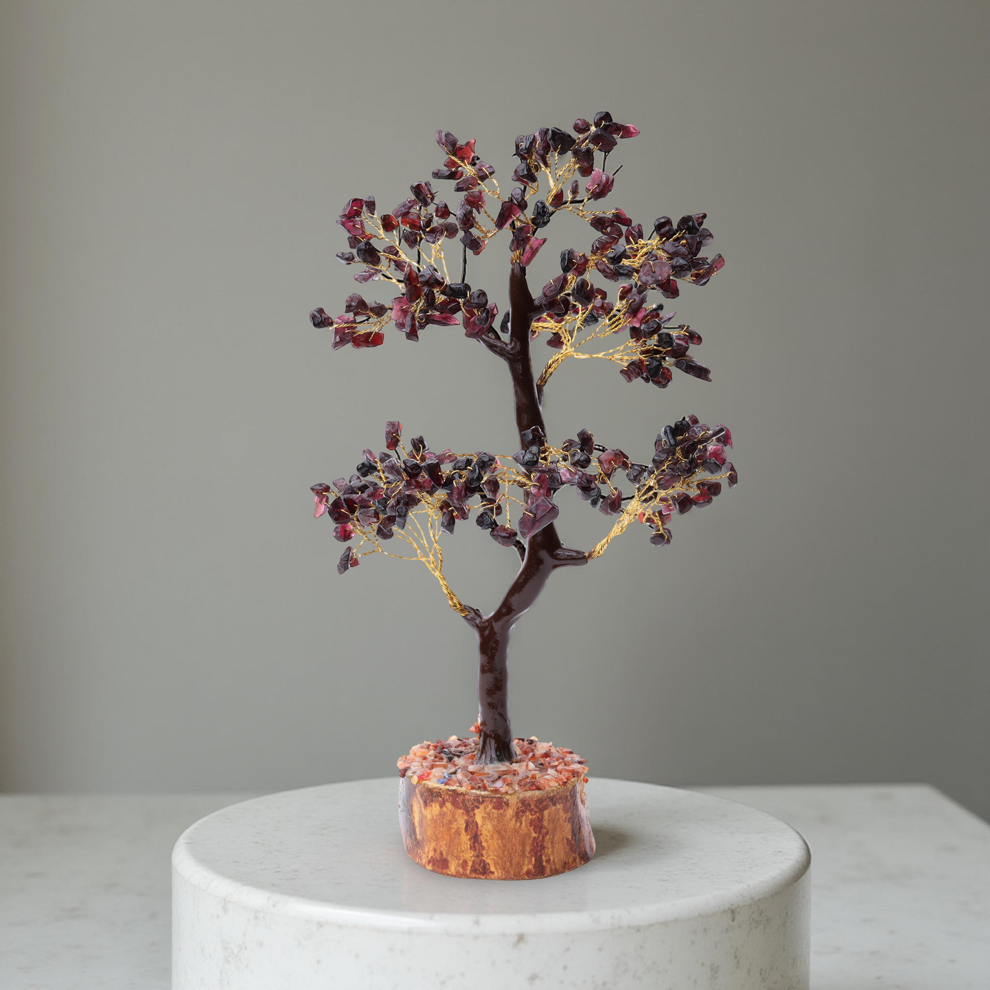 AstroViz deep red garnet stone chip decorative tree on natural wood slice base displayed on white marble pedestal, grey background