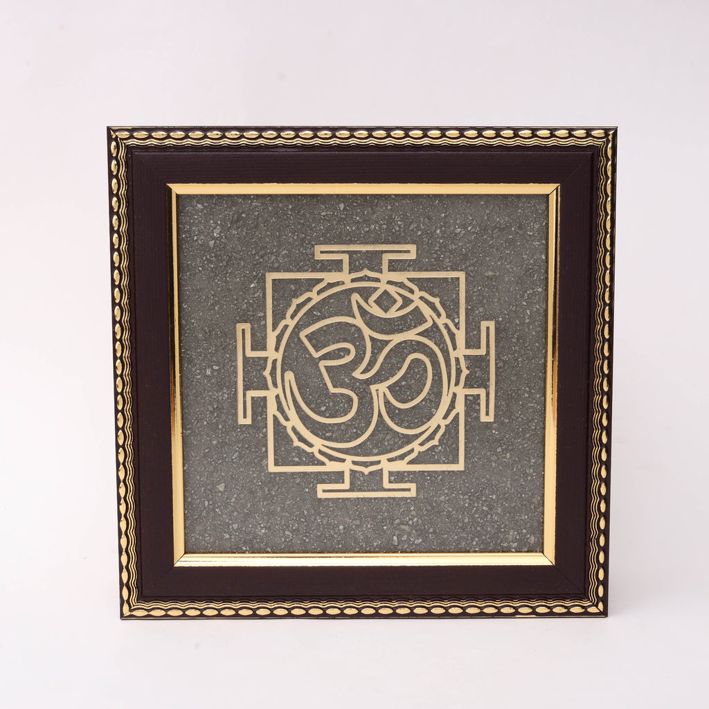 Gold laser-cut Om symbol with Yantra geometric pattern on charcoal stone texture background in dark wood decorative frame.

