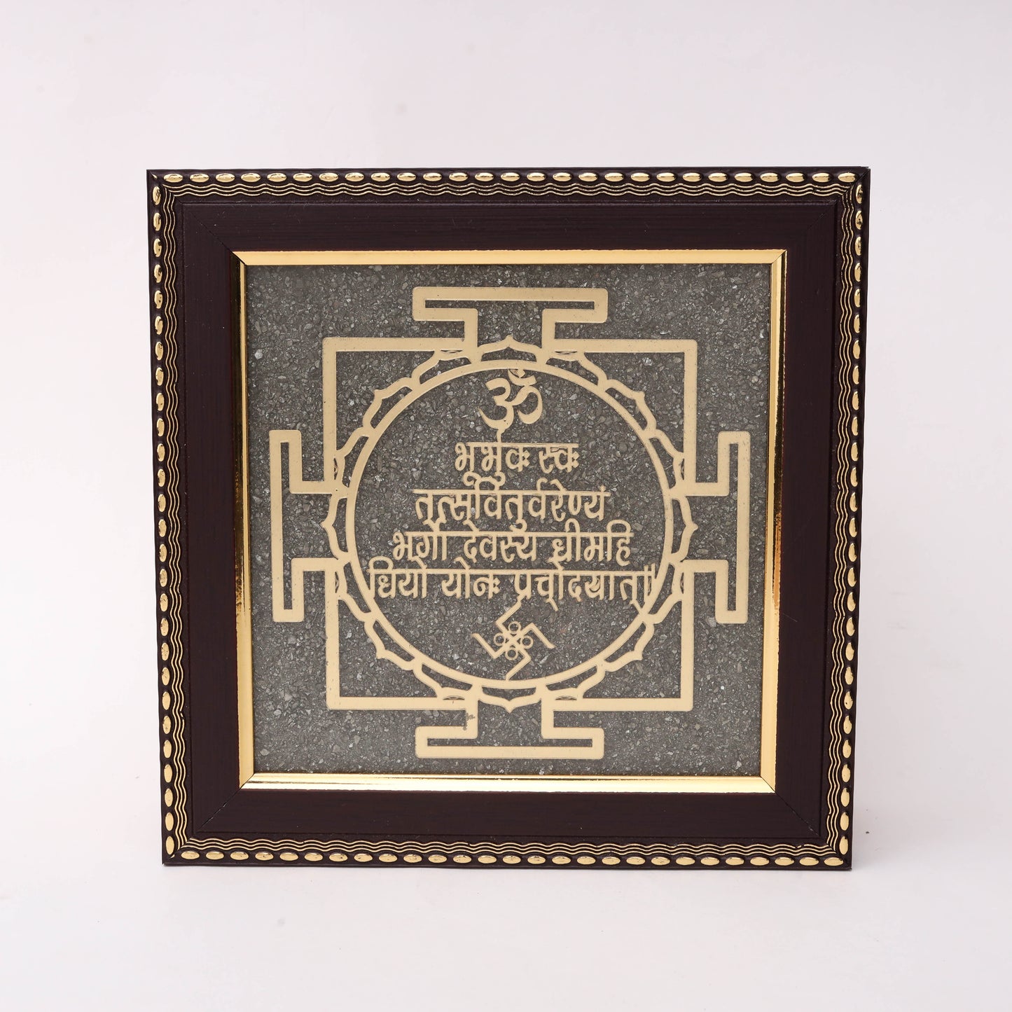 Gold laser-cut Gayatri Mantra Sanskrit text within circular petal border and traditional Yantra square geometry with Om and Swastik symbols on charcoal stone texture background in dark wood decorative frame