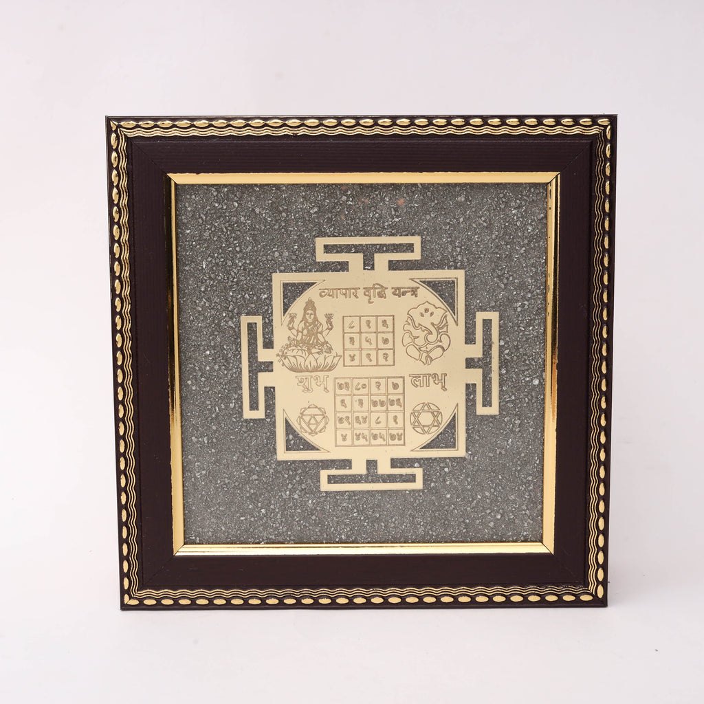 Gold laser-cut Vyapar Vridhi Yantra with Lakshmi Ganesh Shubh Labh numerical grids and Shatkona motif on charcoal stone texture background in dark wood decorative frame