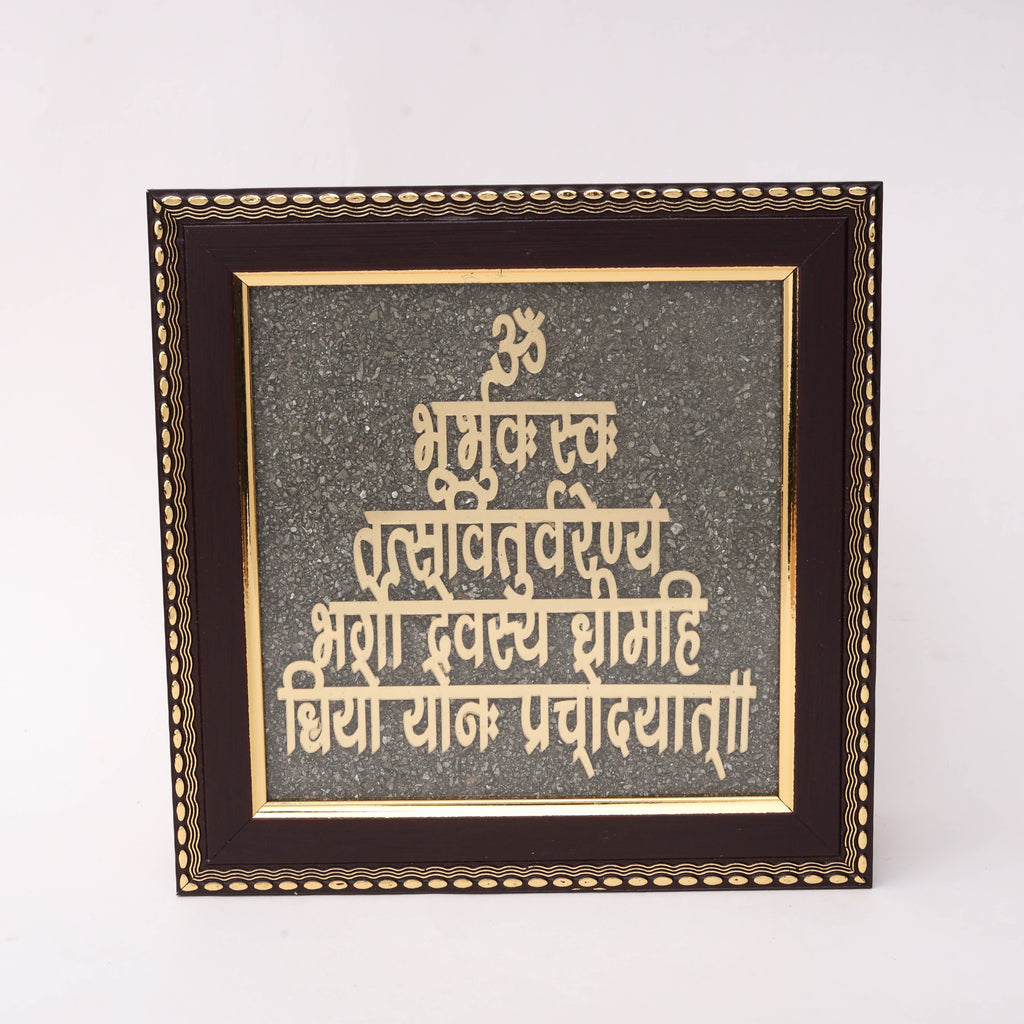 AstroViz Gayatri Mantra gold-tone Devanagari script motif on textured dark grey stone chip background in an ornate wooden frame.
